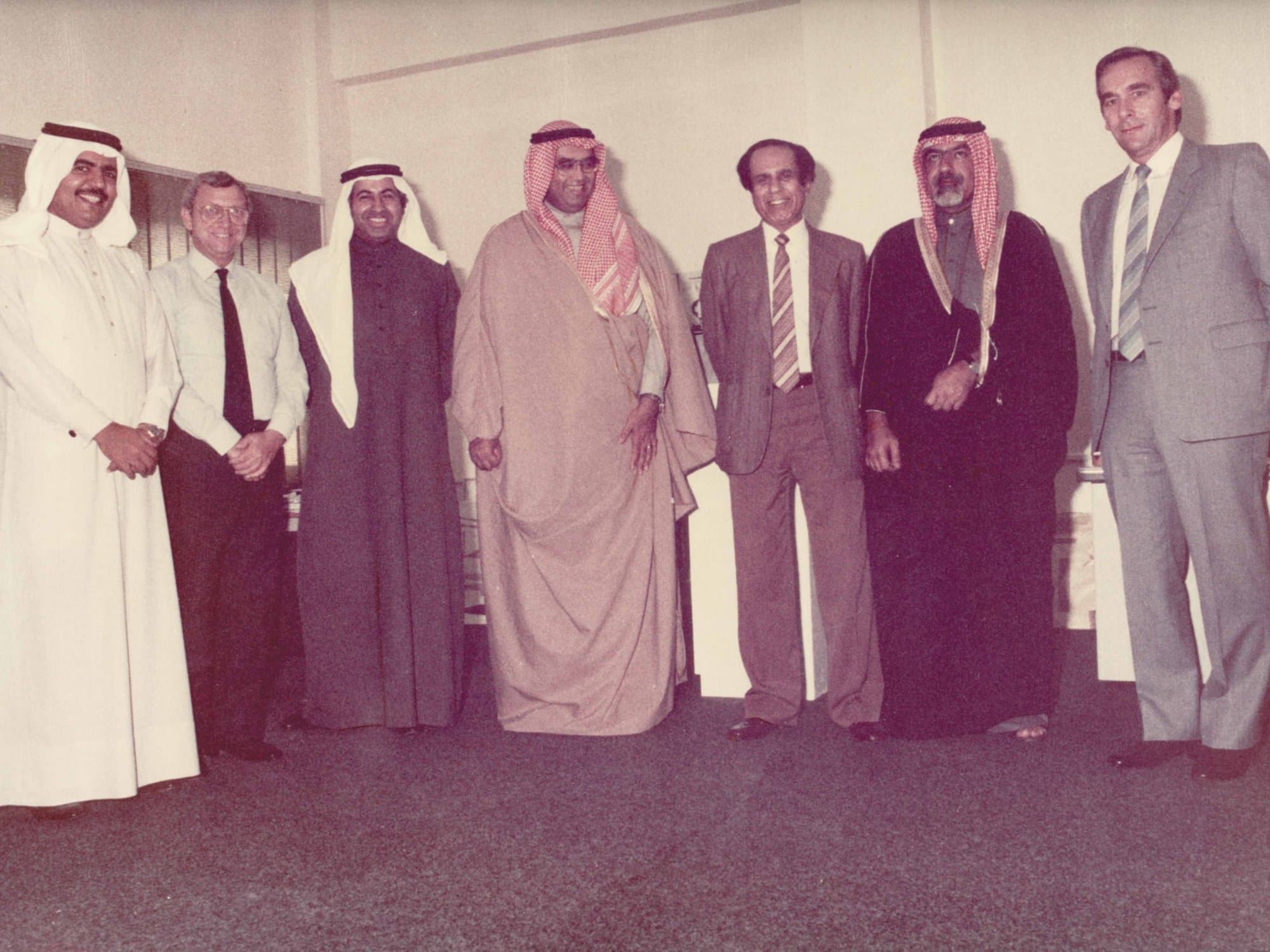 An archive group photograph from the agency's early years, men in Gulf dress and 1970s business suits standing together