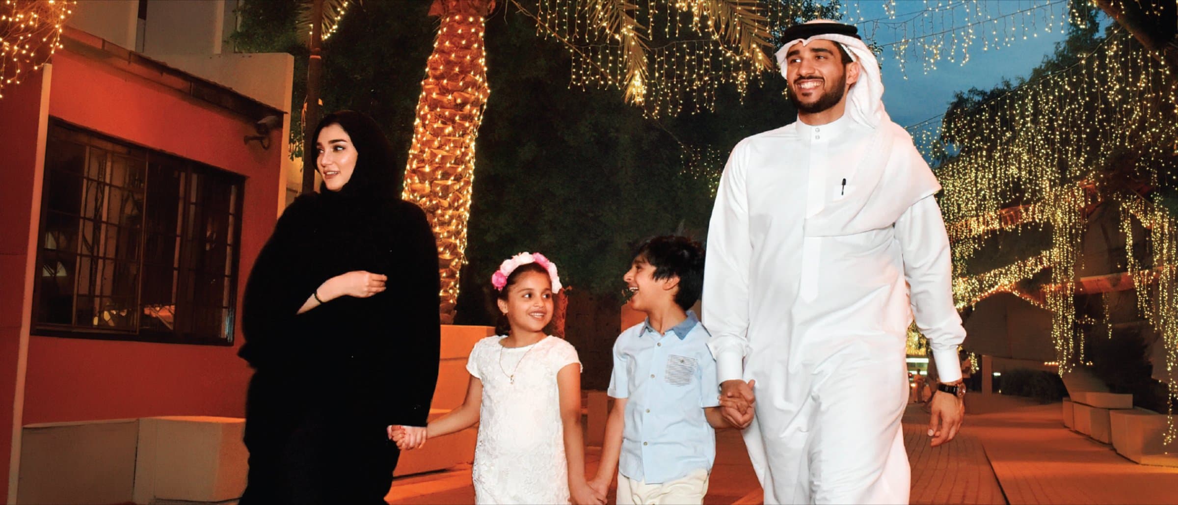 A Bahraini family walking hand in hand along a decorated street at night