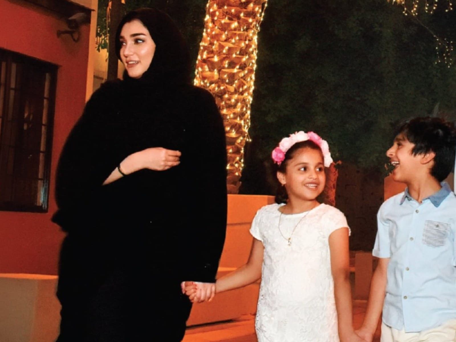 A Bahraini family walking hand in hand along a decorated street at night