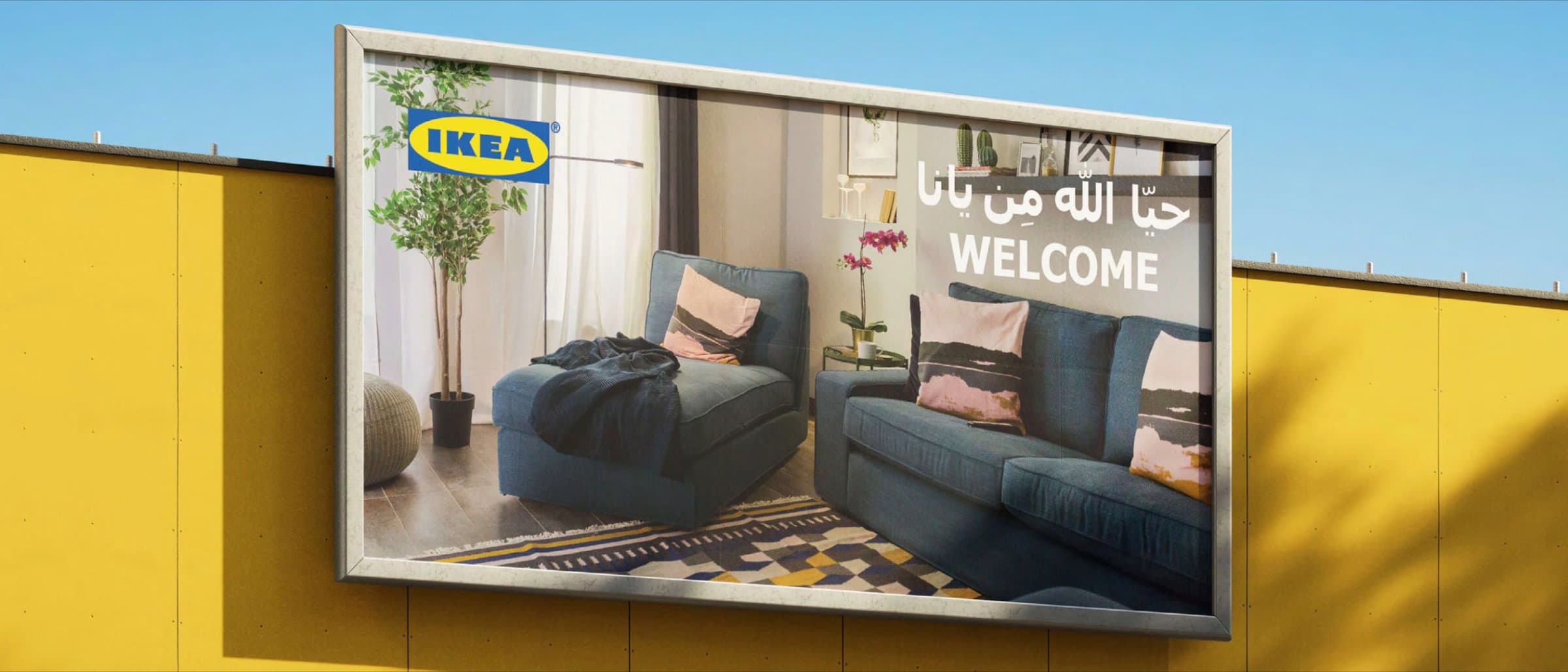 An IKEA Bahrain billboard showing a styled living room with an Arabic welcome message, mounted on a yellow hoarding