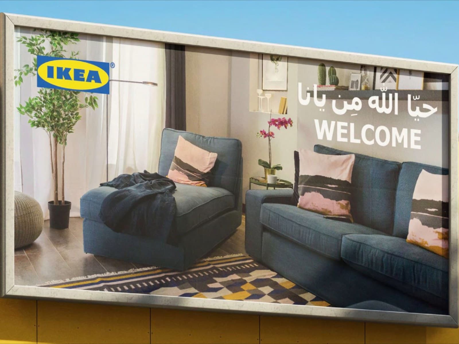An IKEA Bahrain billboard showing a styled living room with an Arabic welcome message, mounted on a yellow hoarding