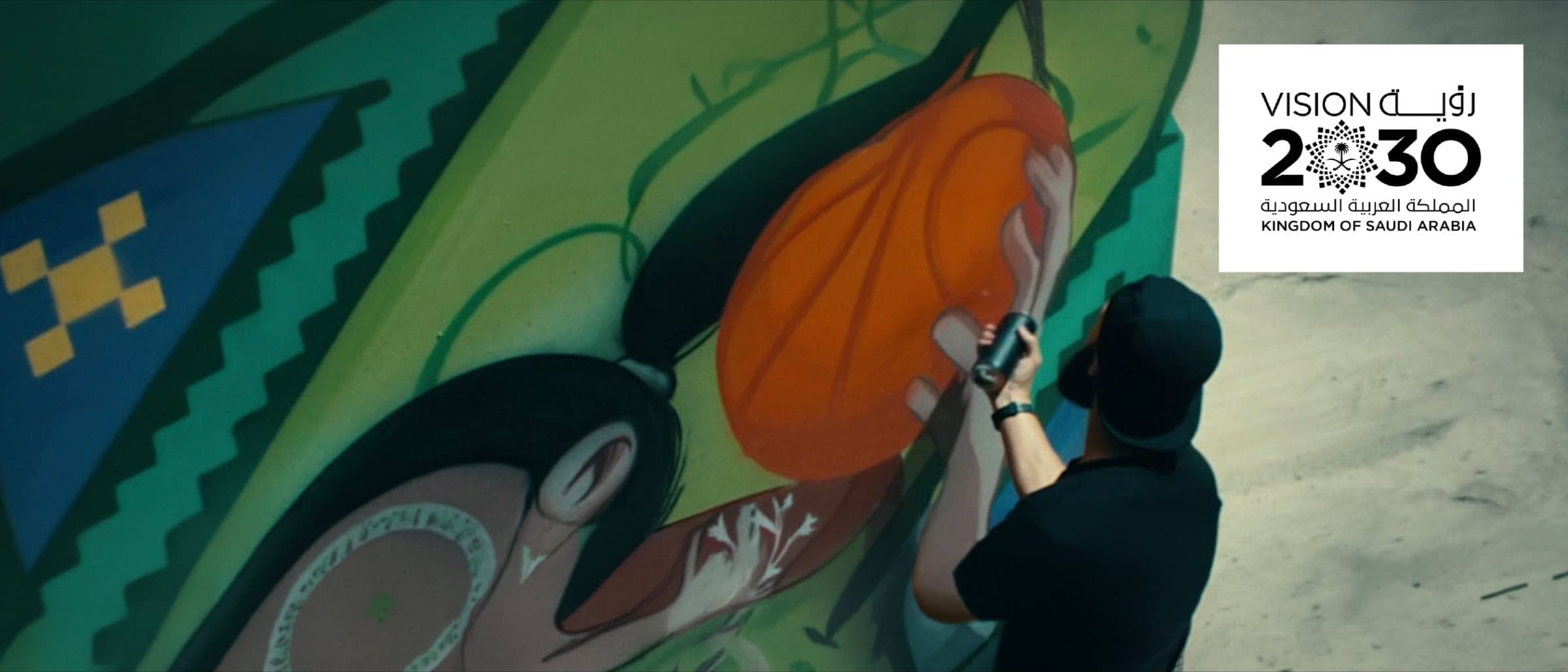 A visitor photographing a large colorful mural, with the Saudi Vision 2030 logo alongside